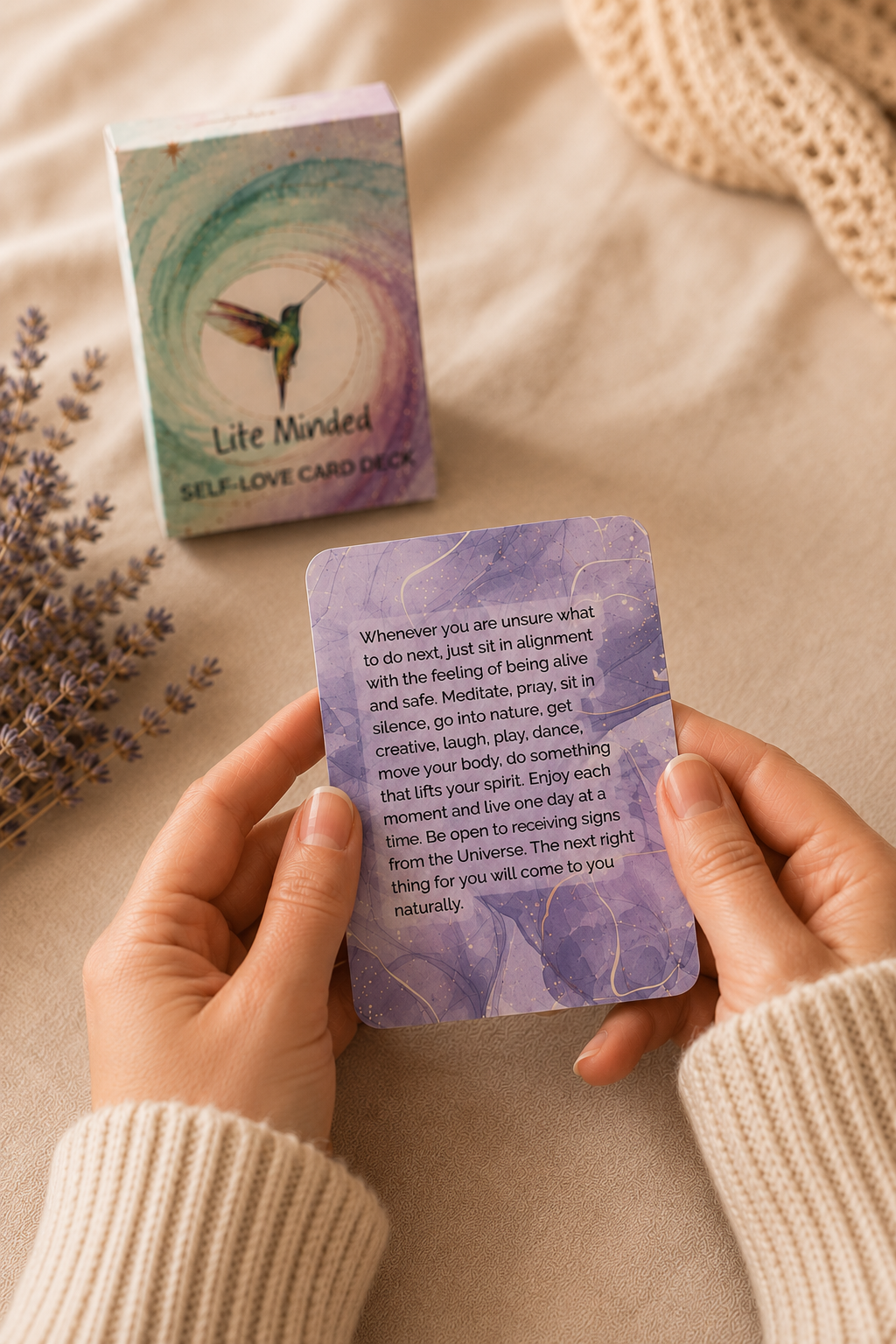 Woman's hands holding a Self-Love affirmation card beside the deck and dried lavender